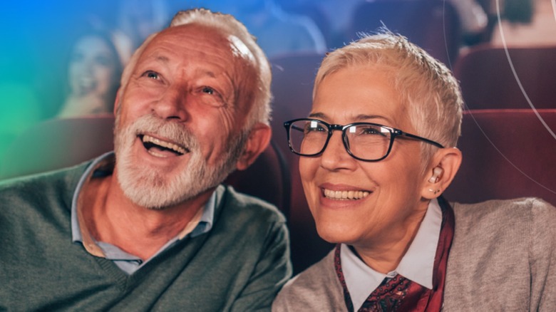 Elderly couple sitting in movie theater, wearing hearing aids