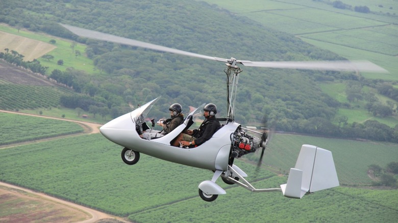 gyrocopter flying over fields with two pilots