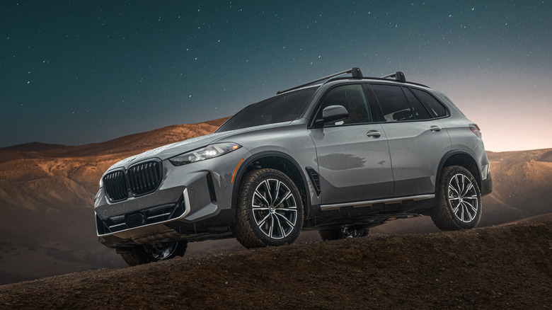 Front 3/4 view of silver BMW X5 parked on mountain under evening sky.