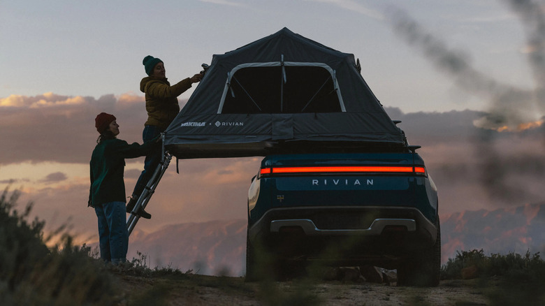 Two people deploy a tent on the roof of a Rivian