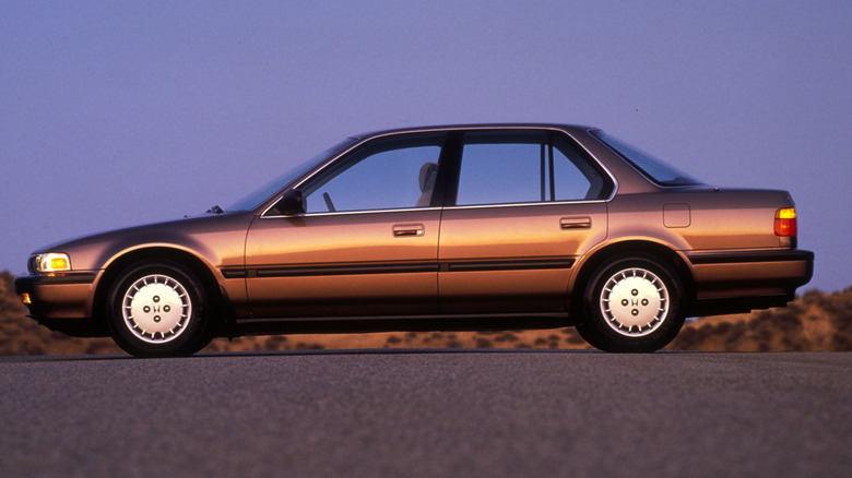 A side view of a golden brown Honda Accord LX on an asphalt road against a magenta sky.