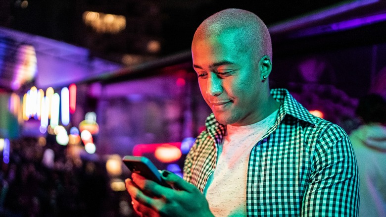 man looking down at phone inside of a club