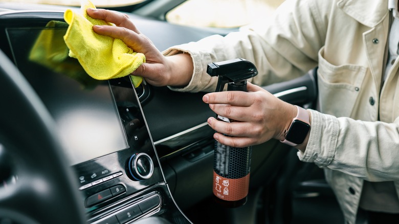 A person cleaning the infotainment system with a cloth and spray