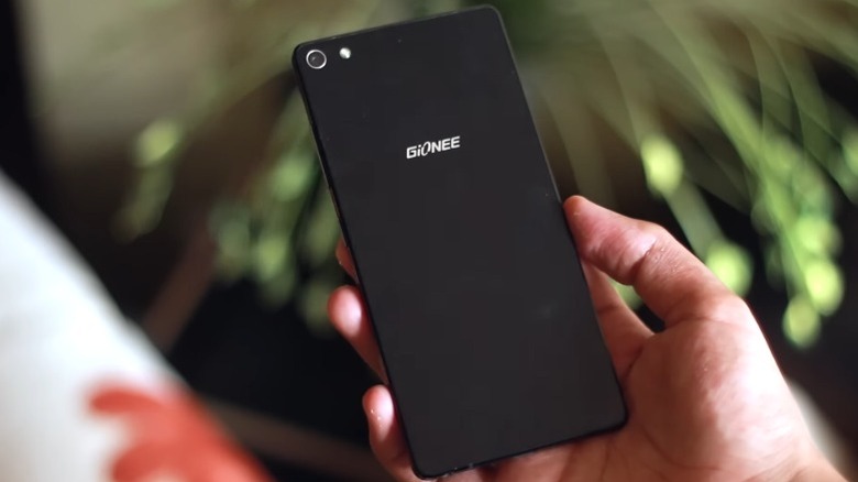 Hand holding a Gionee Elife S7 in front of an out-of-focus plant