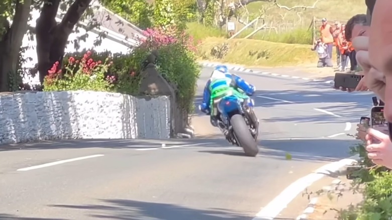 A rider navigating the Isle of Man TT course with roadside hazards visible