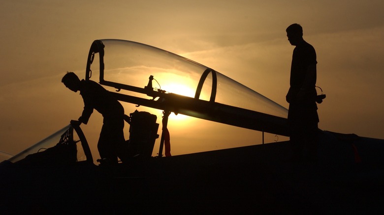 An F-15 Eagle canopy with two personnel working on the aircraft