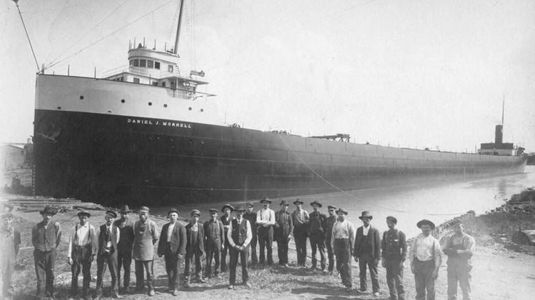 Black and white photo of the SS Daniel J. Morrell with crewman standing on shore in front of her in 1906.