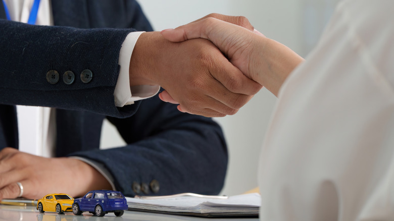 A car dealer and customer shaking hands, two small diecast cars on the table