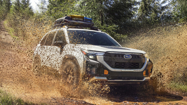 Front 3/4 view of Subaru Forester traversing a mud puddle in forested setting