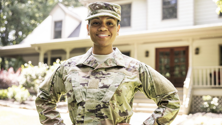 A female U.S. soldier wearing 2023 OCP uniform in front of suburban home