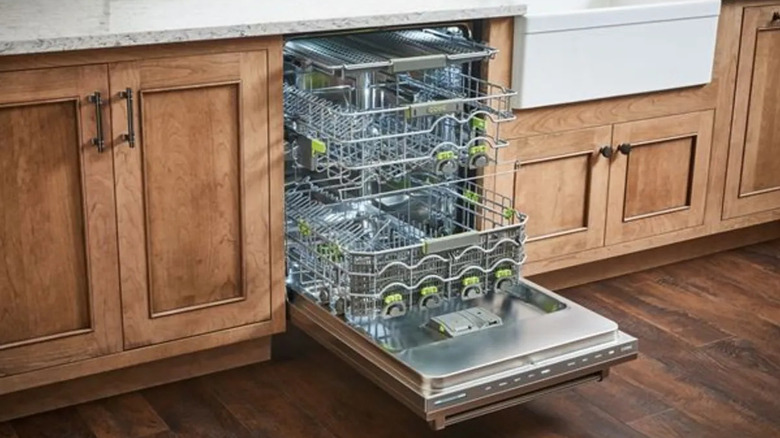 An open Cove dishwasher in a kitchen with wood cabinets and white sink.