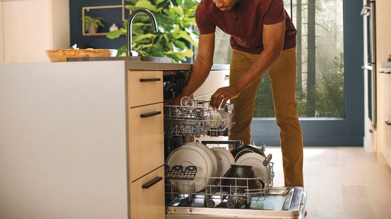 A man loads dishes into an open dishwasher in a kitchen.