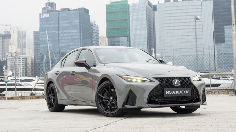 A grey Lexus IS overlooking a line of skyscrapers in Shanghai.