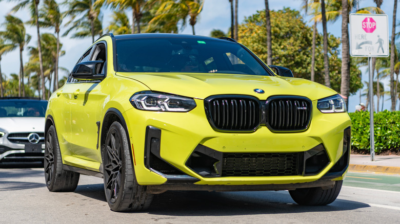 A yellow BMW X4 driving on a road lined with palm trees.