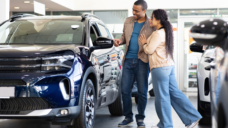 A couple walking through a showroom looking at a car.