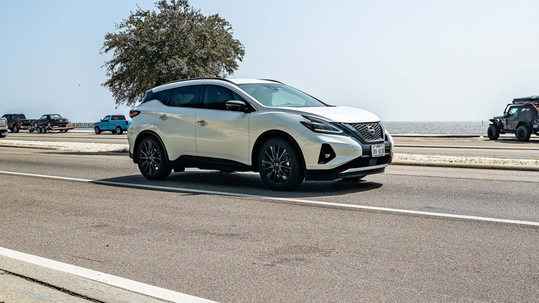 A white Nissan Murano on a road by the sea.