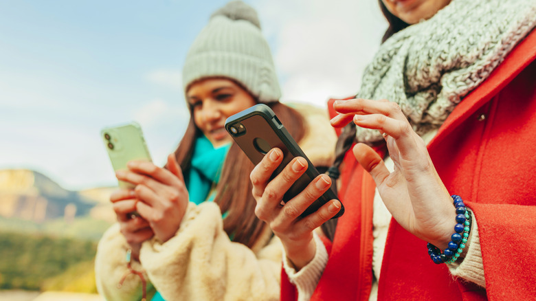 Close up portrait of two young hiker women using iPhones