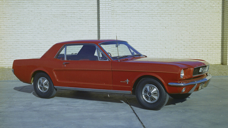 A 1964 Ford Mustang hard-top coupe finished here in a dark shade of red standing in a driveway.