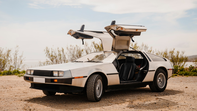 A stainless steel silver DeLorean DMC-12 parked at an angle with its gullwing doors open in the evening.