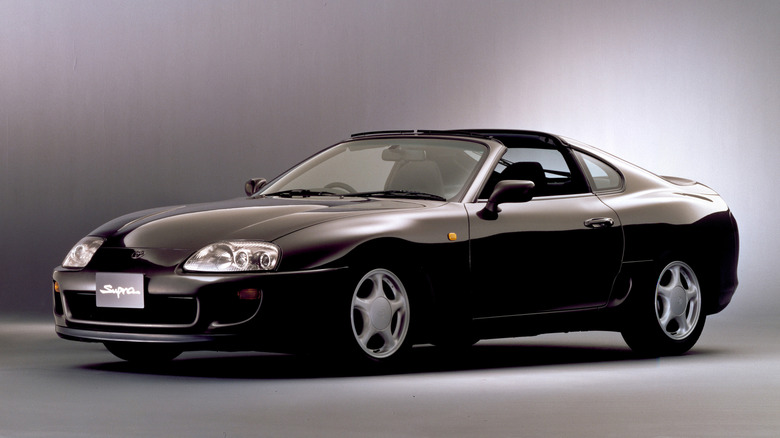 A black 1993 Toyota Supra MkIV SZ Aero Top parked at an angle against a dark studio wall.