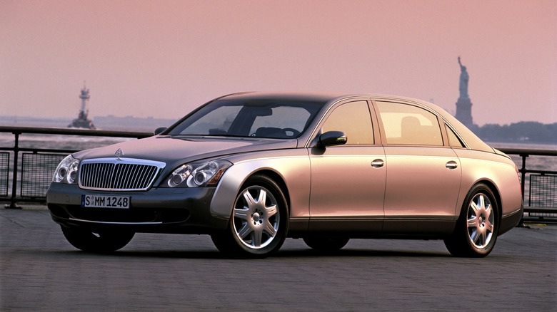 A glossy metallic Maybach 62 executive sedan parked on pavement next to the New York Harbor, with the Statue of Liberty in the back.