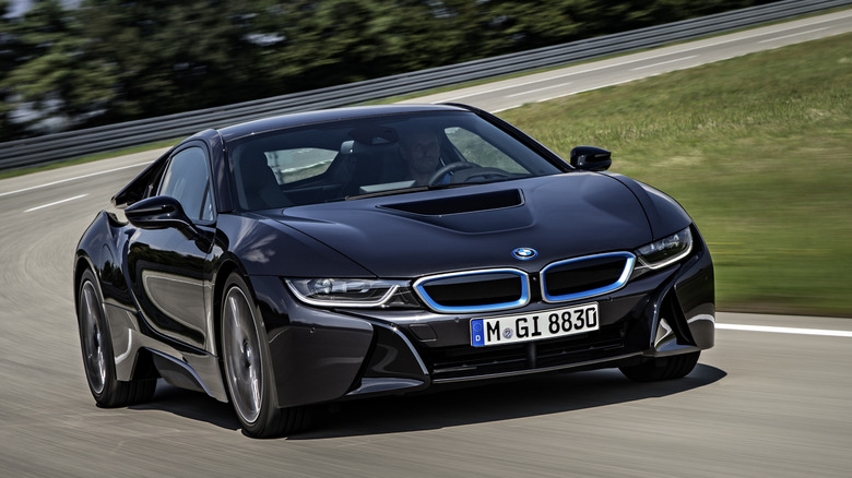 A black BMW i8 sports coupe moving down a racetrack corner at speed in the daytime.