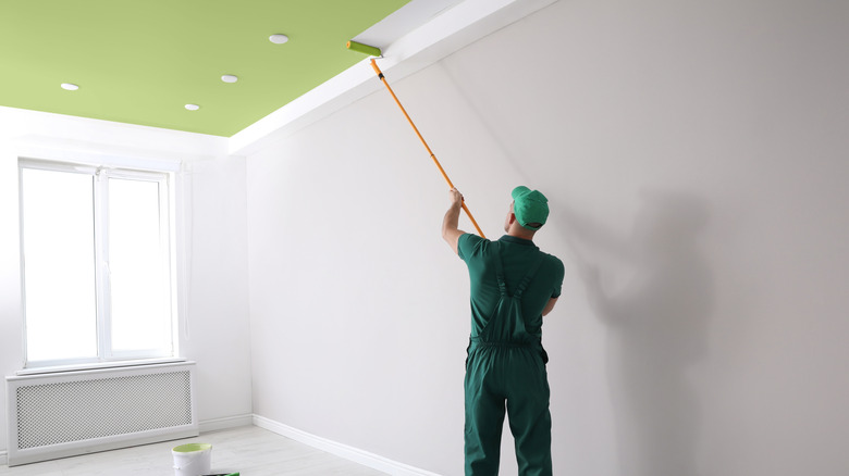 A man using an extension pole to paint his ceiling with green dye