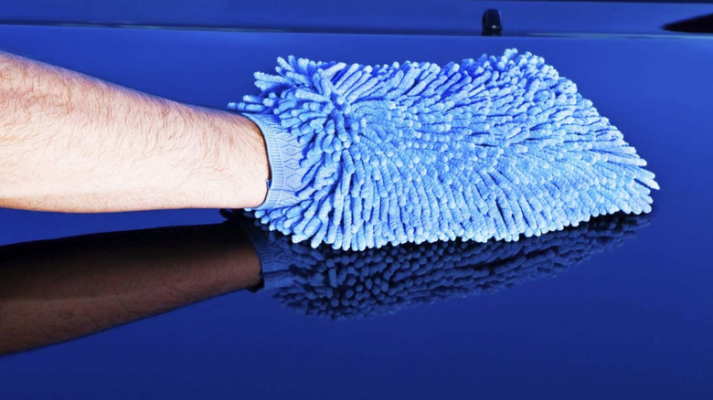 Person washing surface of car using cloth.