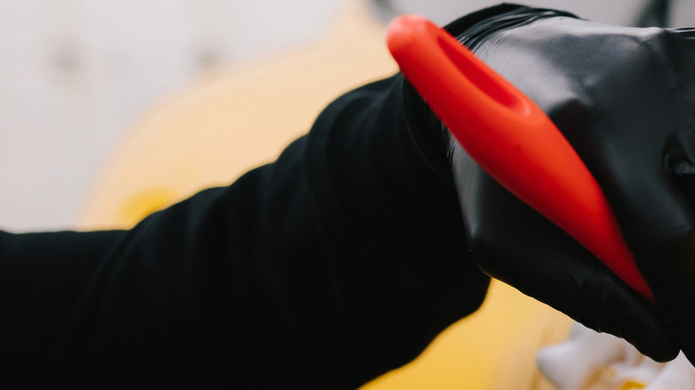 Person wearing gloves cleans the surface of a car with a brush.