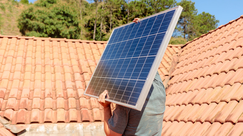 A person carrying a solar panel near a home's roof