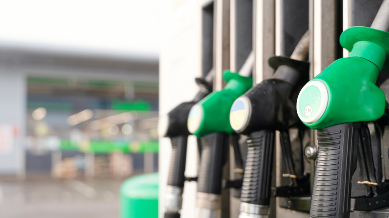 Four filler nozzles, two green diesel fuel nozzles next to black gas nozzles at fuel station, staggered between gas and diesel nozzles