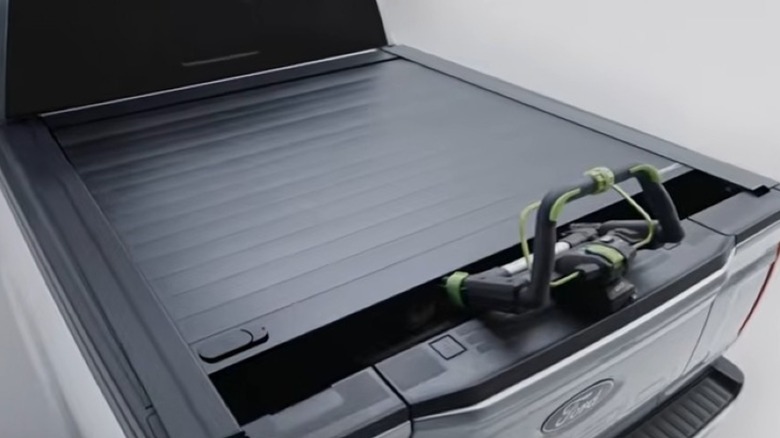 A retractable tonneau cover locked in a partially open position securing a lawn mower inside the truck bed.