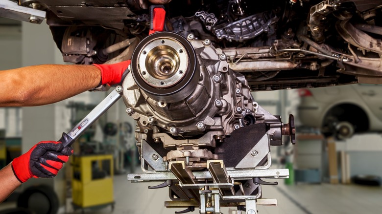 Mechanic dropping transmission out of car in automotive shop