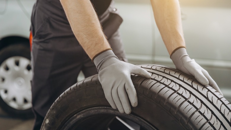 A repair shop worker rolling a replacement tire with his two gloved hands