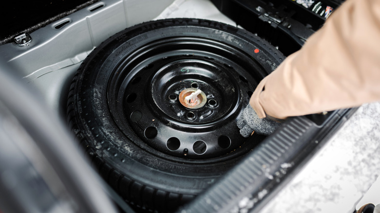 A hand grabbing a donut spare tire from the cargo area of a car