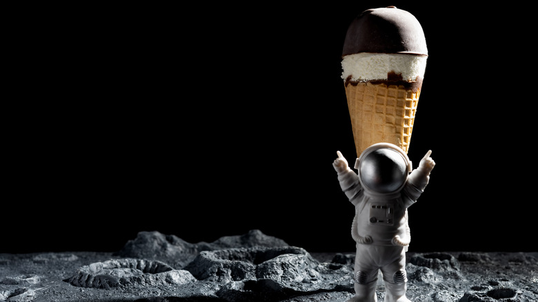 Miniature astronaut standing in front of an ice cream cone on the moon