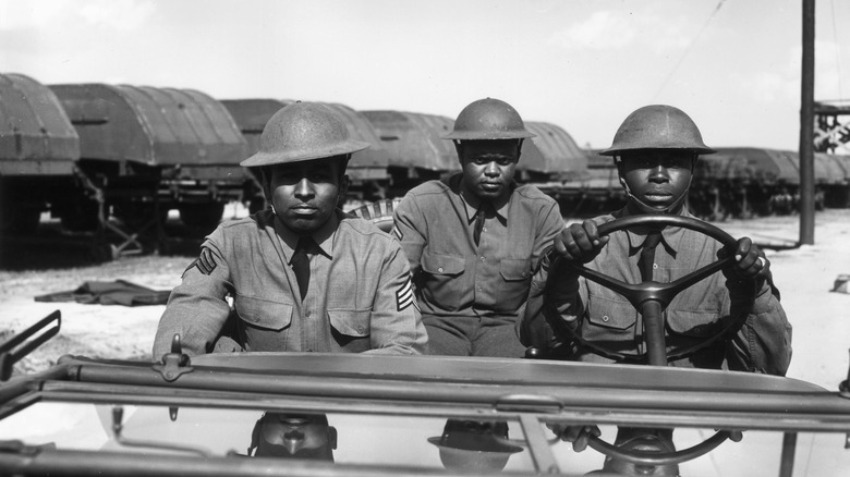Black and white photo of three black soldiers riding in Jeep
