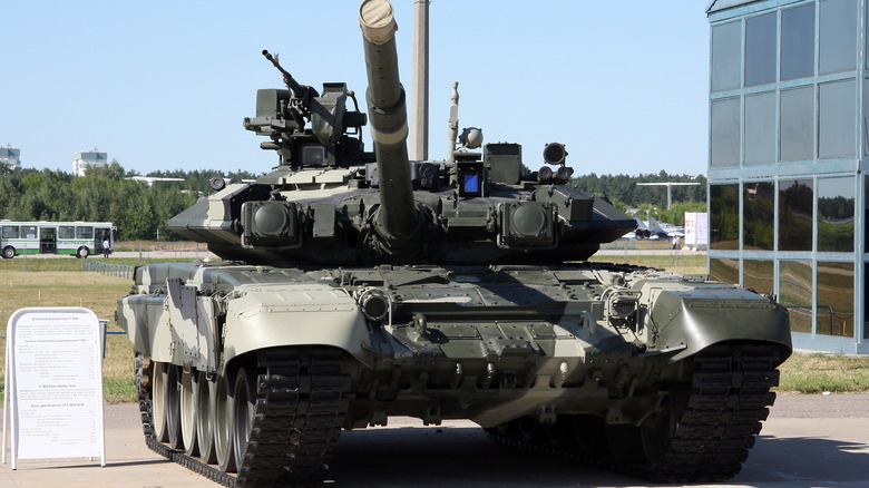 Russian T-90 tank parked outside, next to a glass building.