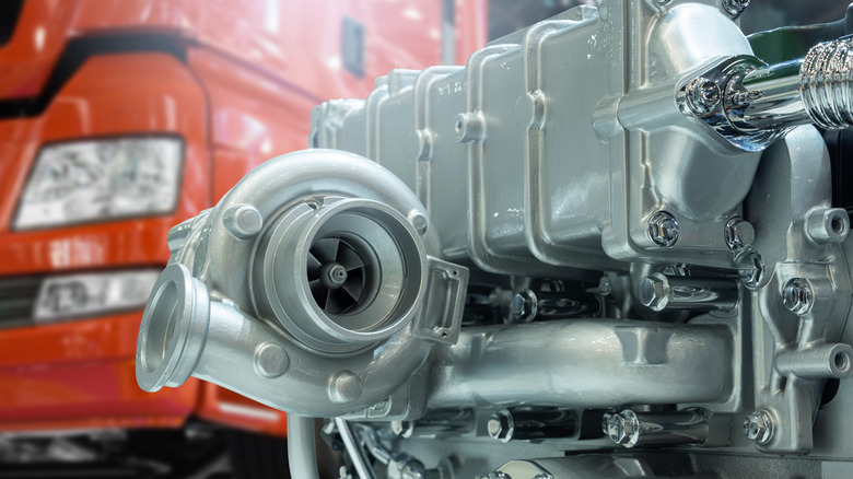 A turbocharger attached to a shiny diesel engine, red European semi truck in the background