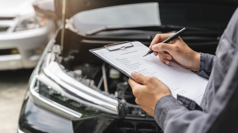 A person taking notes on an unidentified vehicle that has come in for a safety recall