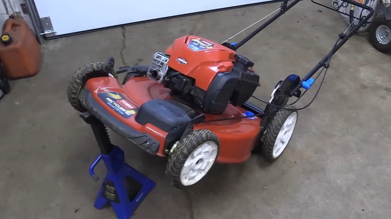 A lawn mower held up with a car jack.