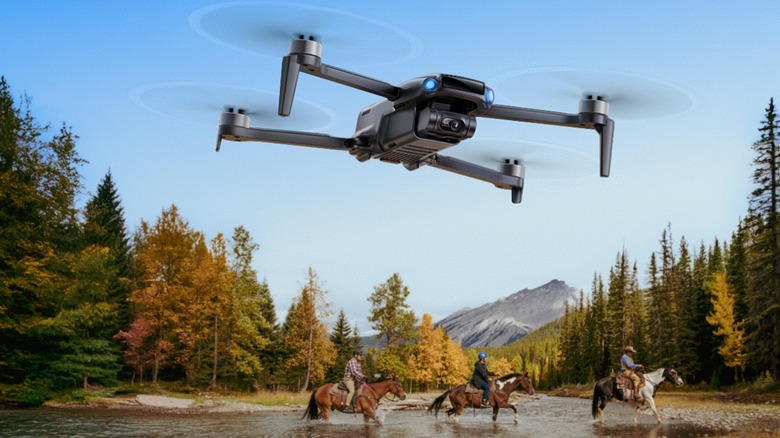 The Ruko U11MINI 4K (RC3) flying over wooded terrain as three people on horseback cross a river.