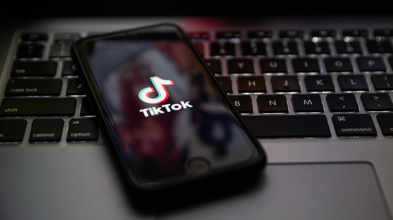 TikTok logo displayed on phone sitting on laptop keyboard. Concept of content moderation.
