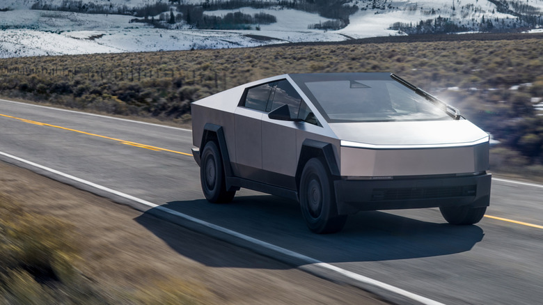 Front 3/4 view of Tesla Cybertruck driving on rural highway with snow.
