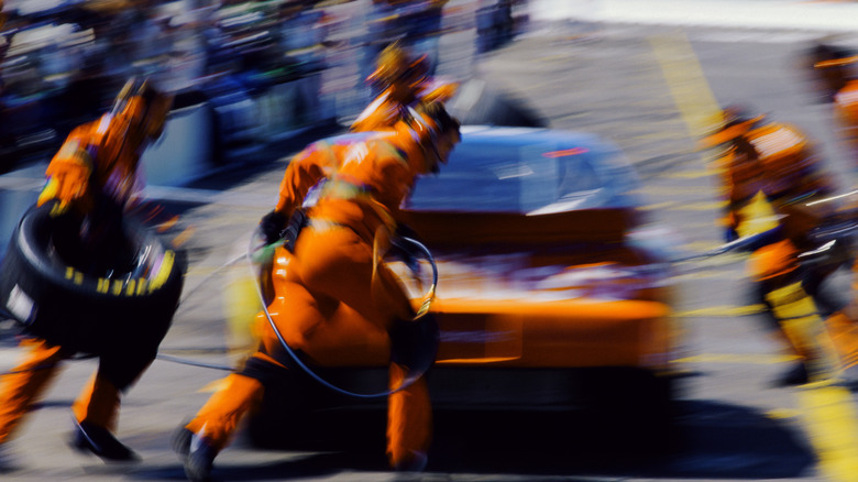 Blurred photo of pit crew sprinting to service rear-right tire of NASCAR stock car, rear-view