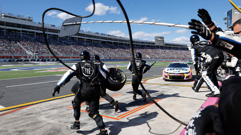NASCAR pit crew readying for an incoming stock car, showing air hoses connected to pneumatic guns