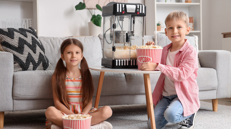 Two little children with popcorn machine at home