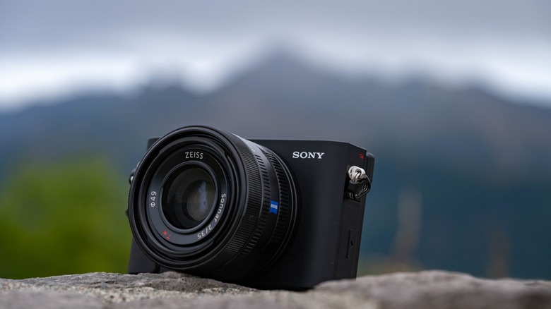 The Sony RX1R iii sitting on a rock with mountains in the bakcground.