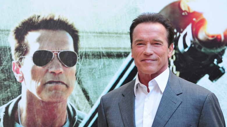 Arnold Schwarzenegger standing next to a movie poster showing his image