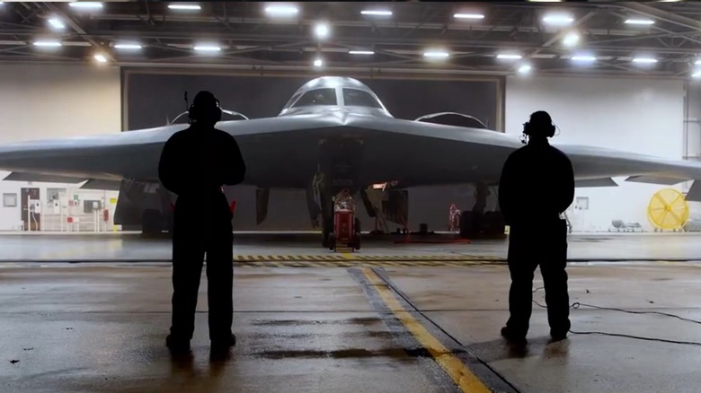 Two ground personnel looking at a B-2 Spirit Stealth Bomber inside its hanger